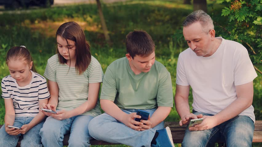 kids and adult on smartphones outdoors, children using mobile phones in a park, family screen time on a bench outside, preteens focused on smartphones in nature, kids browsing phones in a green garden - Powered by Shutterstock - Get 15% off with code: PIKWIZARD15