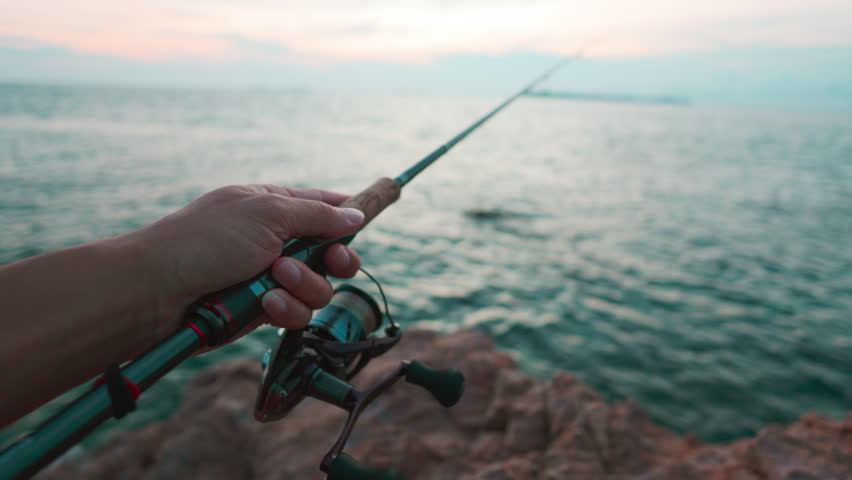 Man hand fishing reel on seashore island sea sport fishing game