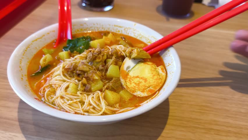Spicy Asian curry noodle soup with misua or vermicelli, egg, and vegetables. Close-up, picking up noodles with chopsticks.