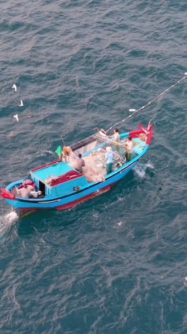 Aerial view of fishing boat on ocean, fishermen working with nets, traditional livelihood and authentic lifestyle of coastal Vietnam. Fishermen pulling nets on wooden fishing boat at sea 