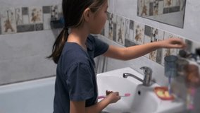 Young Asian girl standing at bathroom sink, squeezing toothpaste onto a pink toothbrush. Morning hygiene, dental care and healthy daily routine concept. - Powered by Shutterstock - Get 15% off with code: PIKWIZARD15