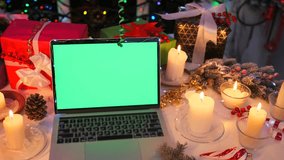 Festive laptop with green screen among Christmas candles, gifts, and pine cones on holiday table. Perfect mockup background for design and seasonal projects. - Powered by Shutterstock - Get 15% off with code: PIKWIZARD15
