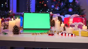 Festive laptop with green screen on table, decorated with pine cones, candles, Christmas tree, and gift boxes in cozy holiday atmosphere. Perfect for mockups and New Year design. - Powered by Shutterstock - Get 15% off with code: PIKWIZARD15