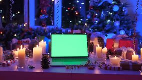 Holiday mockup with laptop on table, green screen for design, surrounded by candles, gifts, pine cones, and Christmas tree in cozy festive atmosphere. - Powered by Shutterstock - Get 15% off with code: PIKWIZARD15
