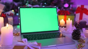 Holiday laptop with green screen placed on decorated table with burning candles, pine cones, gift boxes, and Christmas tree in background. Perfect seasonal mockup template. - Powered by Shutterstock - Get 15% off with code: PIKWIZARD15