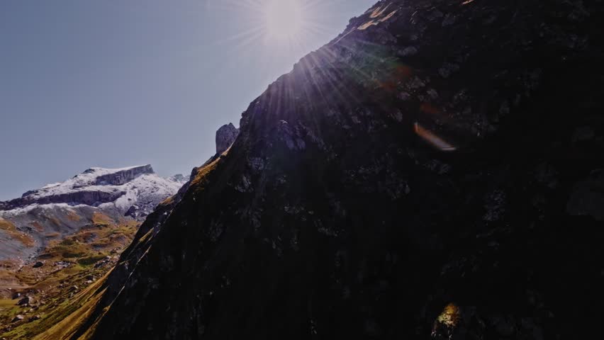 A fast, extreme close-up shot of a steep, rocky mountain climb and a picturesque, stony slope on a sunny day. A racing FPV drone flies smoothly and quickly toward the slope.