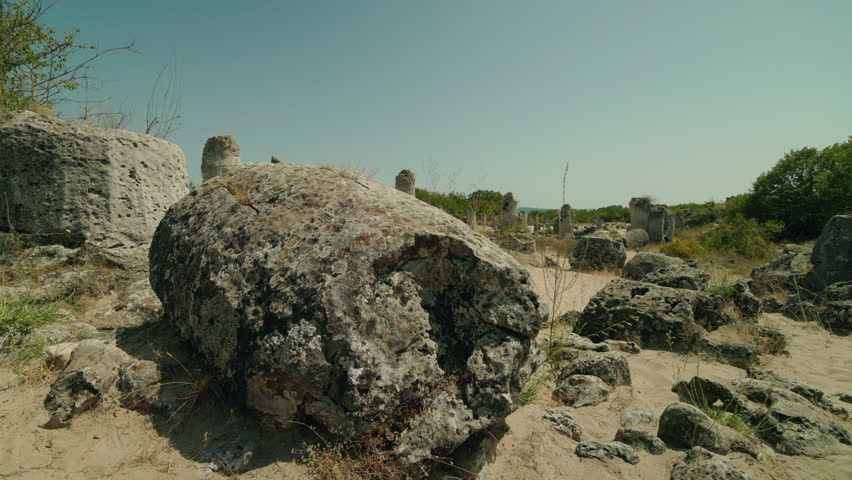 Large limestone boulders and eroded rock formations at Pobiti Kamani in Bulgaria under bright summer sunlight, surrounded by dry sand and sparse vegetation. High quality 4k footage