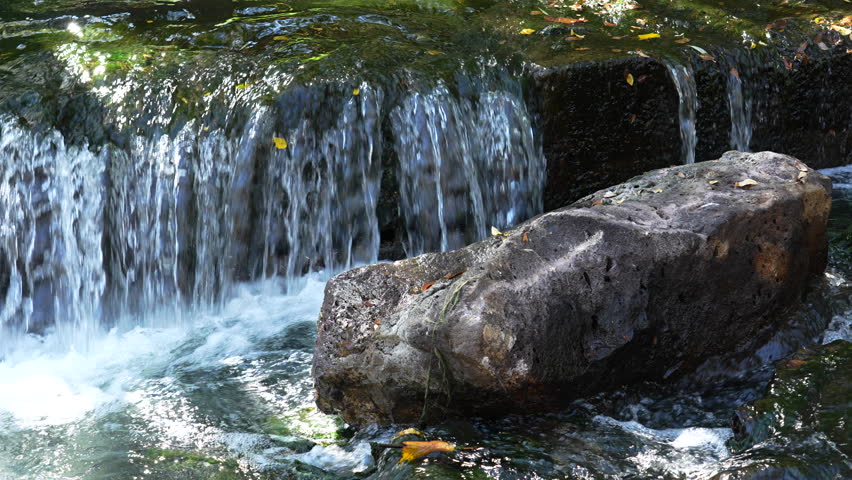 Clear river water flowing over rocks creating small waterfall in nature