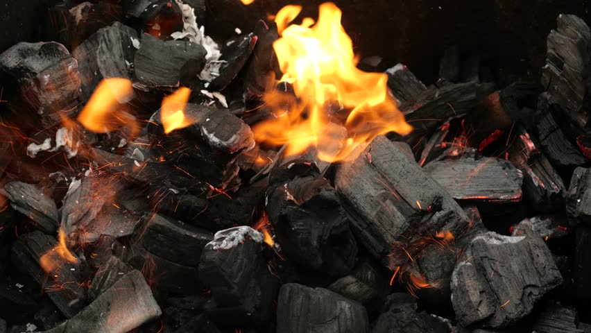 Close-up of charcoal burning in a grill and delicious sausages being grilled