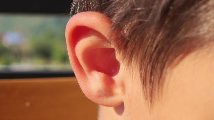 Young boy carefully picking and cleaning inside ear with index finger, focusing on personal hygiene while seated near window with natural illumination