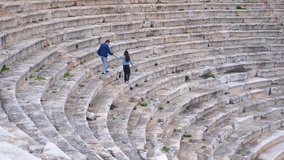 Tourists walking down ancient amphitheater stone steps. Tourists holding hands walking down stone steps of ancient mediterranean amphitheater, revealing historical architecture - Powered by Shutterstock - Get 15% off with code: PIKWIZARD15