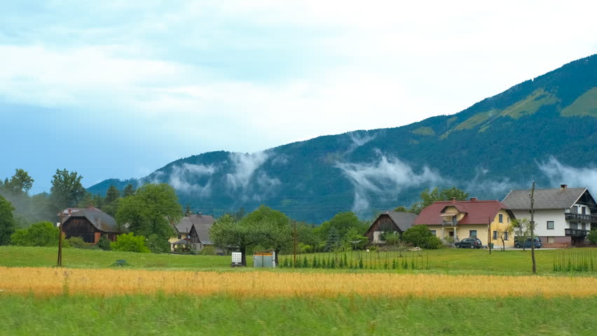 Clouds embracing the countryside near a small village. Low clouds are gently moving over the lush green hills surrounding a picturesque village with traditional houses, creating a serene and scene