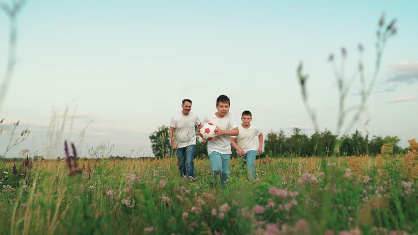 Family, children father runs in park. Children run with ball in park with their father. Children father plays ball on summer lawn. Family jog in park, playing ball outdoors. Boy leads active lifestyle