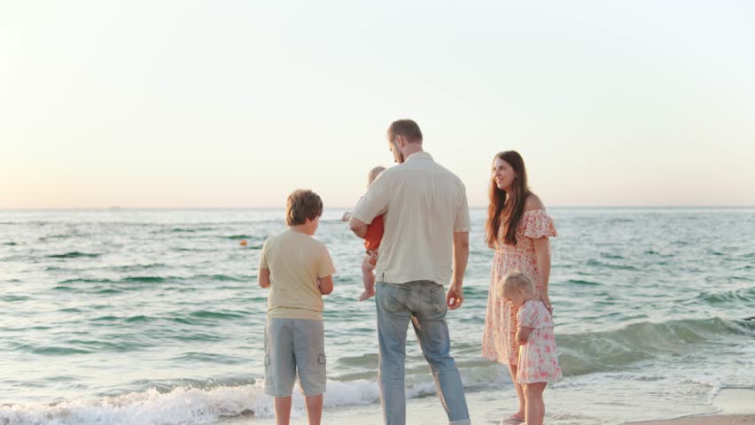 A family is relaxing on the beach during sunset. The parents are engaged with their children, making memories as they explore the shoreline and play in the gentle waves.