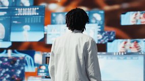 Clinician with arms crossed looking at medical reports on multimedia wall. Doctor wearing lab coat analyses medical research data, monitoring interactive dashboards, camera B - Powered by Shutterstock - Get 15% off with code: PIKWIZARD15