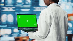 Chroma key laptop used by clinician looking at medical reports on multimedia wall. Doctor wearing lab coat analyses research data on green screen notebook, monitoring dashboards, camera B closeup - Powered by Shutterstock - Get 15% off with code: PIKWIZARD15