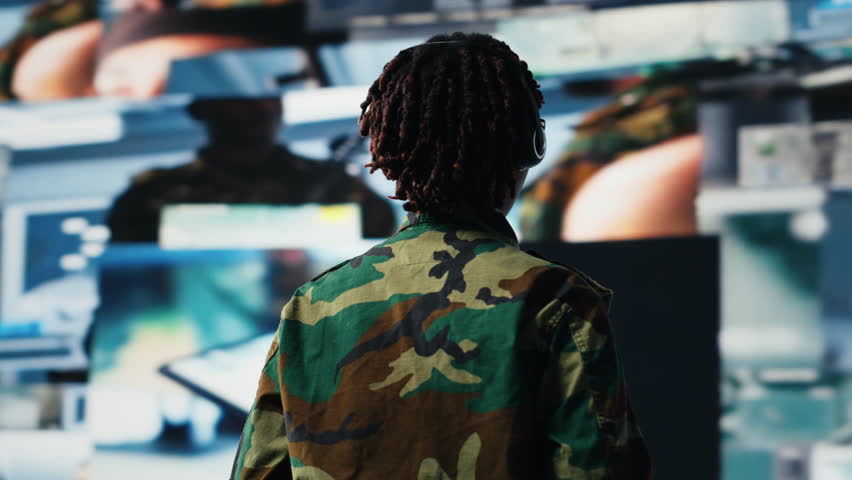 Military commander in war communicating enemy activity to troops, following them using videowall. Military dispatcher wearing headset speaking about enemy threats seen on digital display, camera B