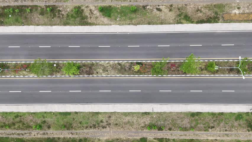 Aerial top-down drone view of a multi-lane highway with light traffic, showing motorcycles and a truck driving through a rural area.