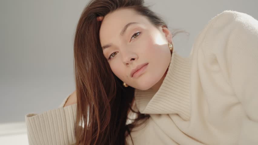 Beautiful young brunette woman with beige sweater and pants posing at studio. Woman having smooth healthy skin. Laughing happy woman. Fashion model with beautiful eyes. Face lifting, cosmetics.