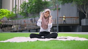 Asian Muslim woman enjoy music with headphones while sitting in the city. Attractive young girl wearing hijab feel happy and relax, having picnic and listen to songs outdoors in modern urban setting. - Powered by Shutterstock - Get 15% off with code: PIKWIZARD15