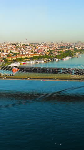 Vertical video. Istanbul, Turkey. Golden Horn Bridge and Halic Metro Station with pedestrian crossing illuminated by morning sun over bay. Aerial View, MasterShots, Dronie. Rich colors
