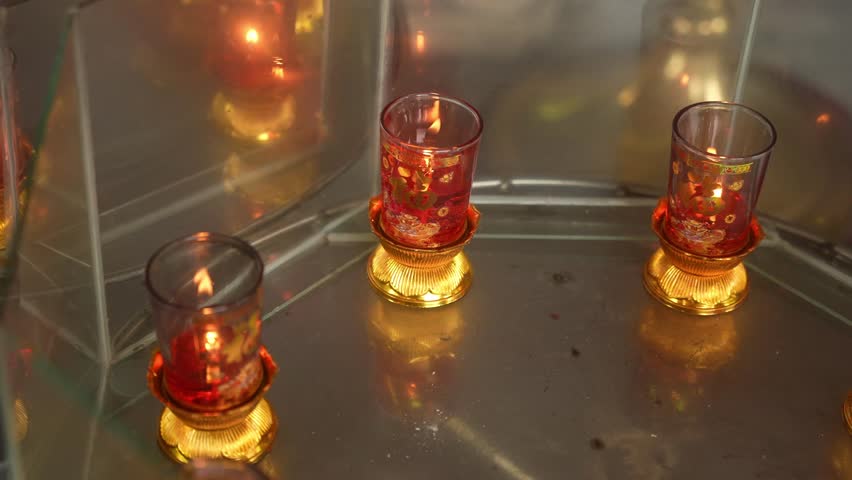 A close static angle holds throughout, framing three lit glass candle holders with red and gold floral designs. Their flames flicker gently, mirrored on the reflective metallic surface below. - Powered by Shutterstock - Get 15% off with code: PIKWIZARD15