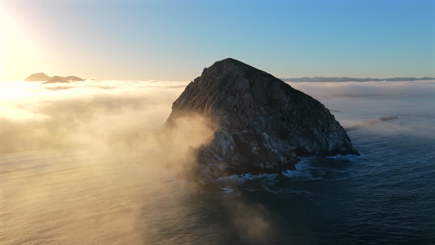 Breathtaking aerial view showcases a stunning Morro rock island at dawn, beautifully enveloped in soft blanket of mist and gentle waves, highlighting the magnificence of nature, Morro Bay, California