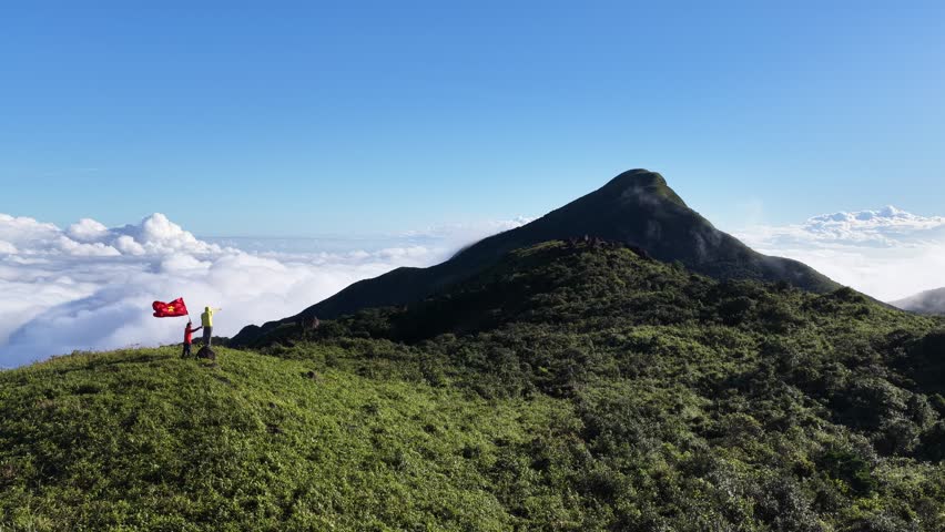 QUANG TRI, VIETNAM – OCTOBER 3, 2025: A happy couple waves a Vietnamese flag on a mountain summit above a sea of clouds, celebrating their achievement.