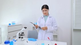 A young Asian female scientist holds a clipboard and a test tube filled with blue liquid, carefully reviewing experiment data related to science, laboratory, scientist, experiment, and research. - Powered by Shutterstock - Get 15% off with code: PIKWIZARD15