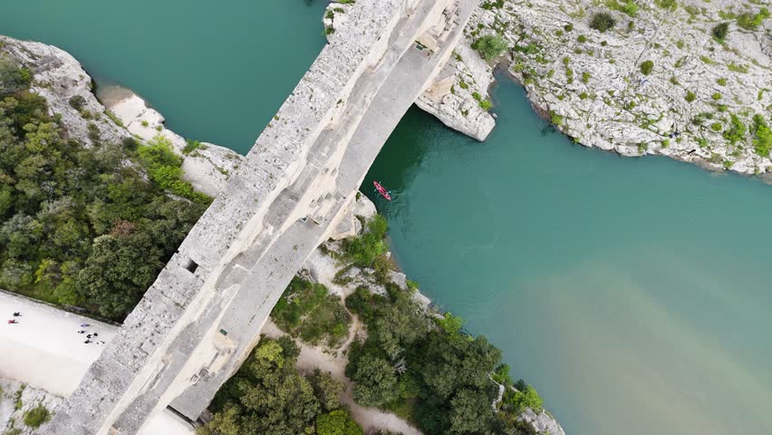 Drone glides above Pont du Gard, revealing its monumental scale contrasted with tiny figures below