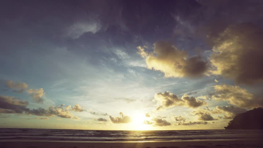 The sky is a beautiful mix of blue and orange hues, with clouds scattered throughout. The sun is setting over the ocean, casting a warm glow over the water. The scene is serene and peaceful