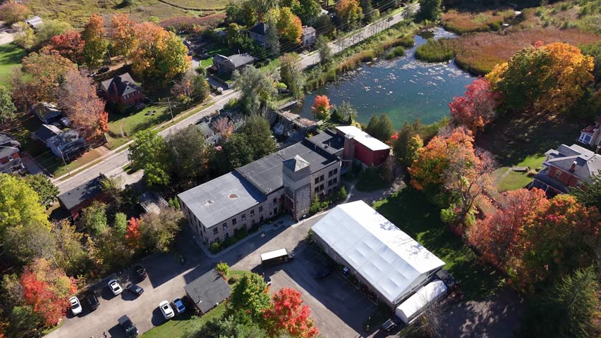 A detailed aerial view of the historic Alton Mill Arts Centre in Ontario, Canada. The shot showcases the stone building and its surroundings in peak autumn colour.