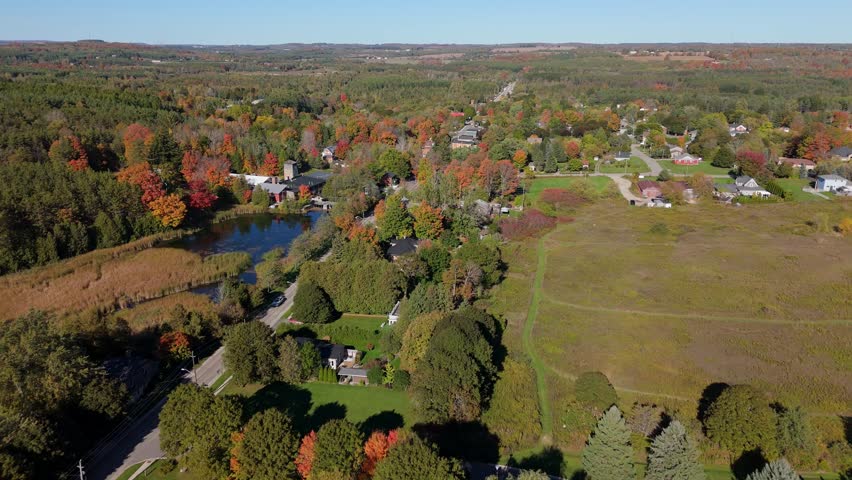 A beautiful, wide aerial shot of the village of Alton, Ontario, and its surrounding rural landscape, showcasing the stunning colours of the autumn season from a high altitude.