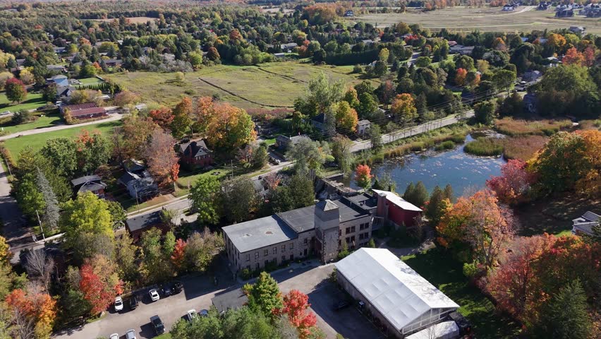 A beautiful aerial drone shot of the historic Alton Mill Arts Centre in Ontario, Canada, showcasing the building and its scenic surroundings during peak autumn.