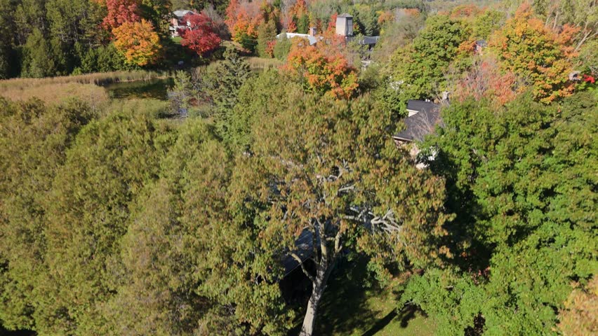 A stunningly picturesque aerial view of the historic Alton Mill in Ontario, Canada. The mill and its tranquil pond are surrounded by a forest ablaze with spectacular fall colours.
