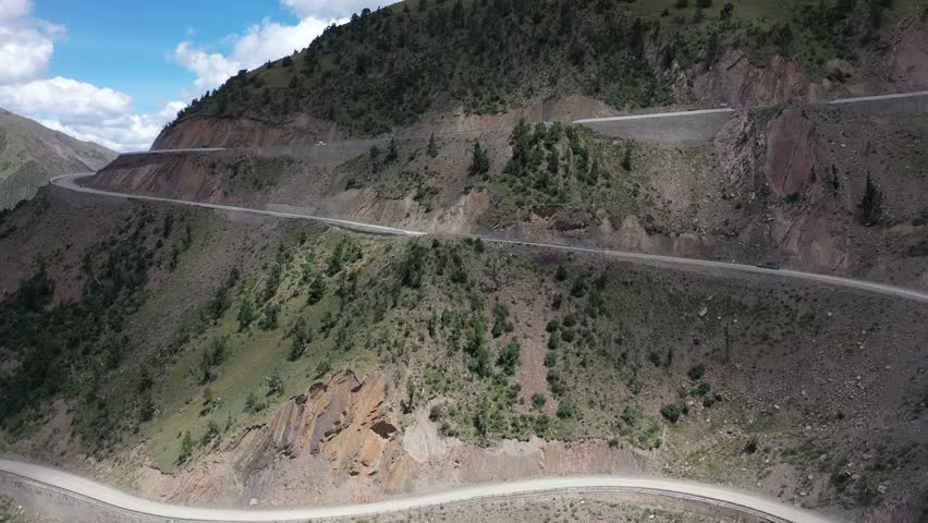 Aerial view of winding mountain highway through rugged Tibetan landscape with dramatic curves and steep terrain under cloudy blue sky