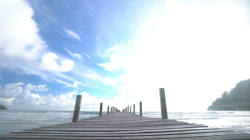 A pier with a wooden walkway leading to the water. The sky is blue with a few clouds