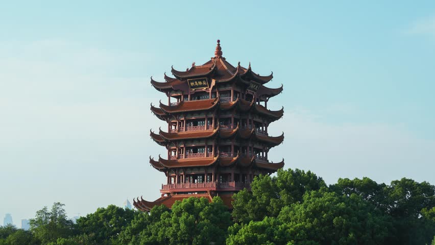 Traditional Chinese pagoda tower with multiple tiers and curved roofs surrounded by lush green trees against blue sky, showcasing ancient architectural heritage.