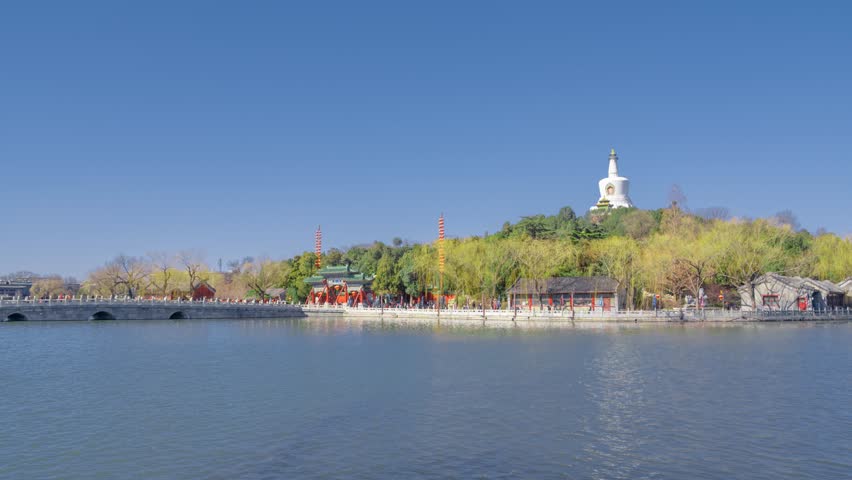 Beautiful spring view of Beihai Park in Beijing with white pagoda, lake reflections, and streaming crowds enjoying the scenic waterfront during equinox season.