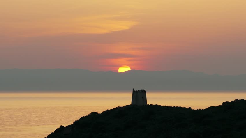 San Macario island and tower with setting sun in background, Pula, Sardinia, Italy. Aerial drone lateral view