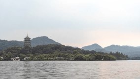 Evening view of Leifeng Pagoda and West Lake in Hangzhou, China with misty mountains and calm waters reflecting the scenic landscape during golden hour time lapse. - Powered by Shutterstock - Get 15% off with code: PIKWIZARD15