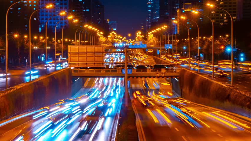 Night time lapse view of busy Beijing traffic with dense light trails flowing through urban highway interchange and city skyline with illuminated skyscrapers - Powered by Shutterstock - Get 15% off with code: PIKWIZARD15