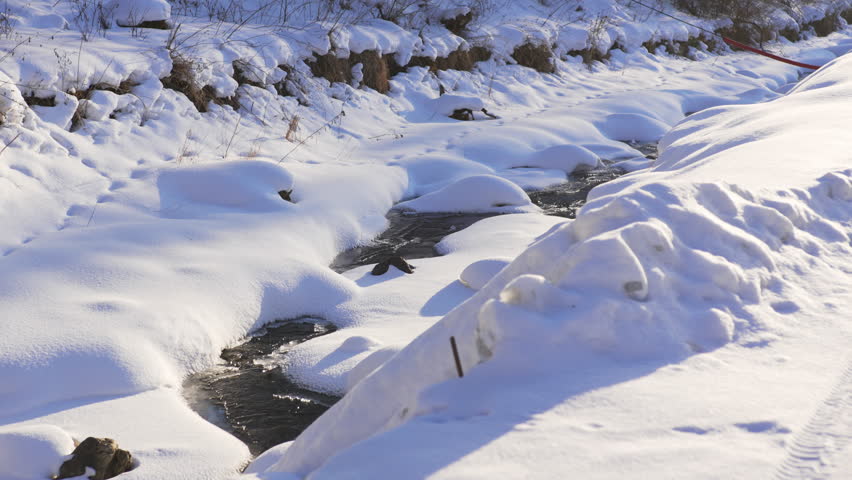 Bright sun melts snowy slopes forming clear sparkling streams. Scene shows transition between frozen winter and warm spring awakening