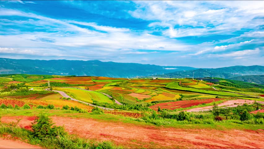 Colorful terraced farmland with red soil and vibrant agricultural fields in Yunnan Province, China, showcasing traditional farming methods against mountain backdrop.