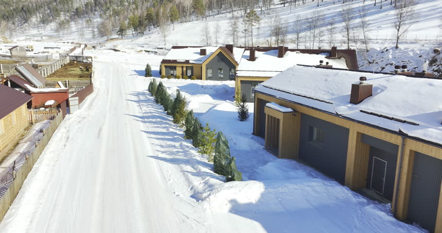 Cozy cabins clearly outlined against snowy wooded mountains. Composition merges warmth of human architecture with majestic alpine wilderness