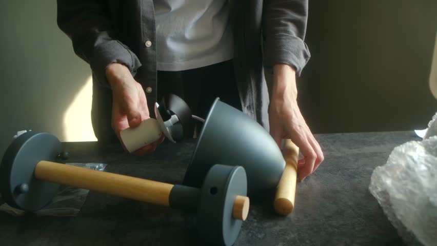 Female hands assembling a modern designer chandelier with wooden details for home interior renovation, carefully following the instructions and putting together the stylish light fixture