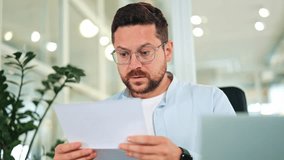 Worried businessman, dressed in a light blue shirt, processes upsetting news from a document in a bright office. Stressed specialist expresses frustration and disappointment with financial results. - Powered by Shutterstock - Get 15% off with code: PIKWIZARD15
