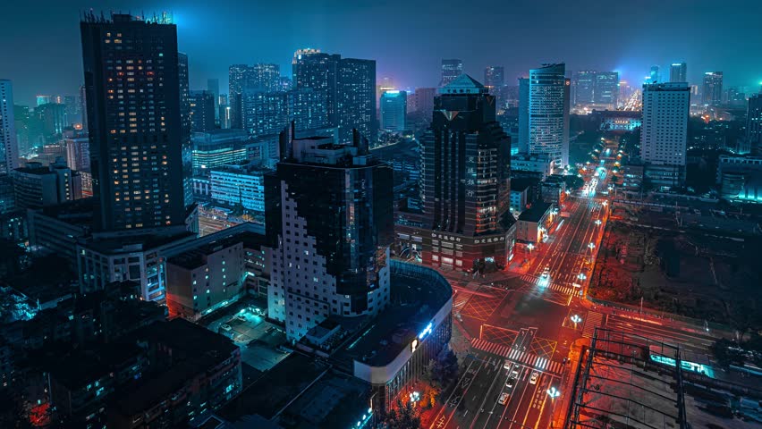 Night time lapse aerial view of Chengdu city center with illuminated skyscrapers, busy traffic light trails, and glowing urban plaza in China