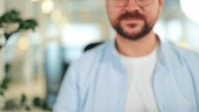 Successful man, smiling broadly, wearing a blue shirt and glasses, proudly holds up shiny house keys with a house keychain in a bright modern interior. Excited and happy about home ownership. - Powered by Shutterstock - Get 15% off with code: PIKWIZARD15