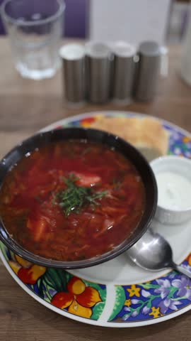 Traditional borscht soup served in a bowl with fresh dill sour cream and bread on a colorful plate warm homemade meal with rich beet flavor and cozy cafe atmosphere inviting comfort